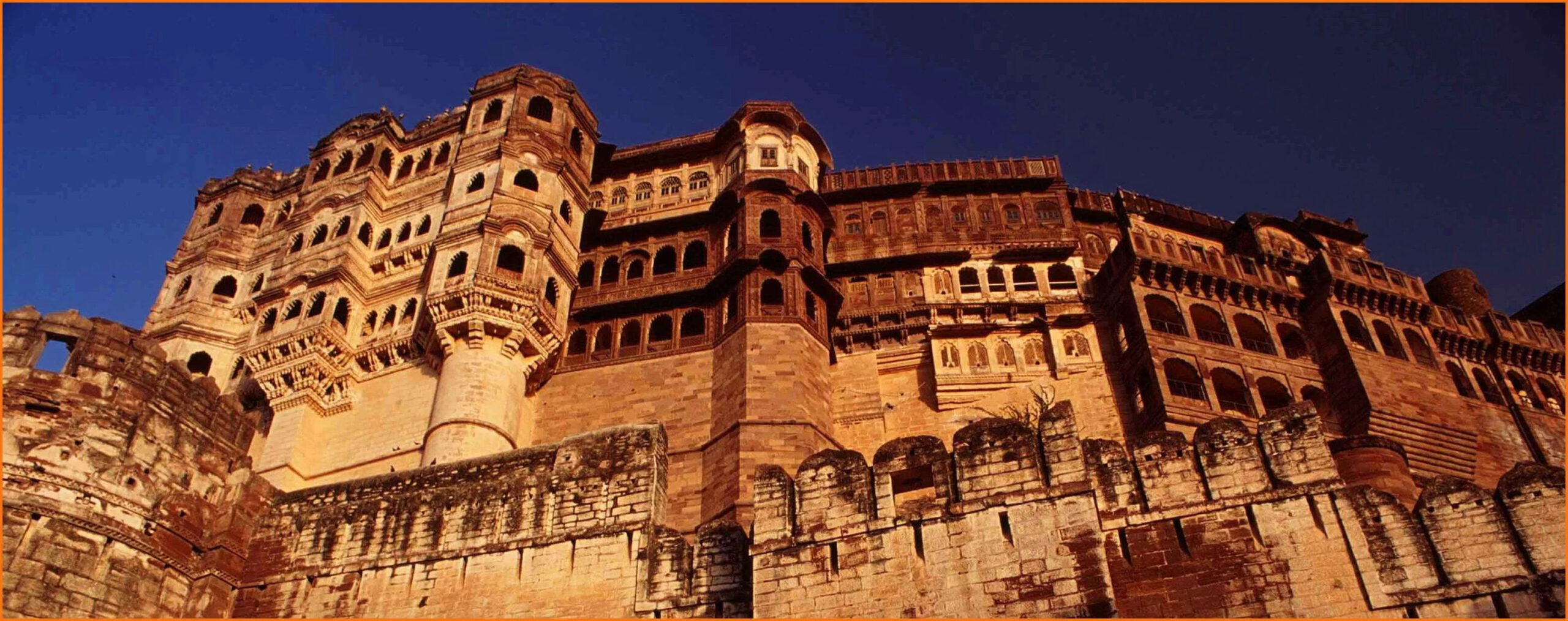 Large sandstone hilltop fort with carved balconies and arched windows under a blue sky