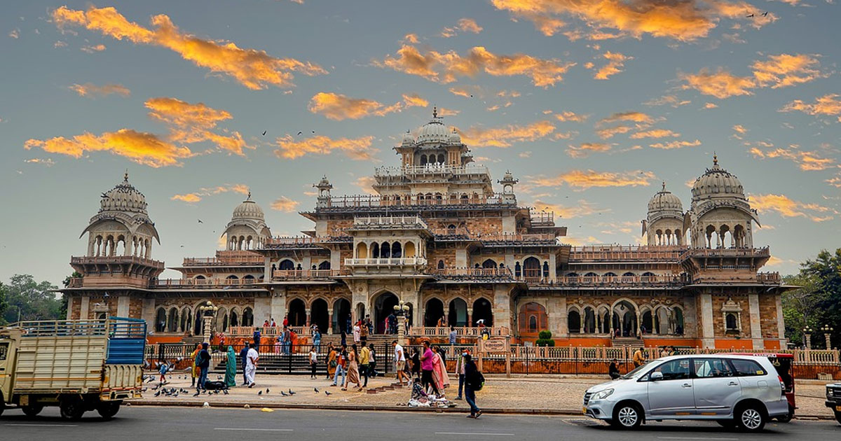 Albert Hall Museum in Jaipur at sunset, with visitors, pigeons, and traffic passing on the road in front