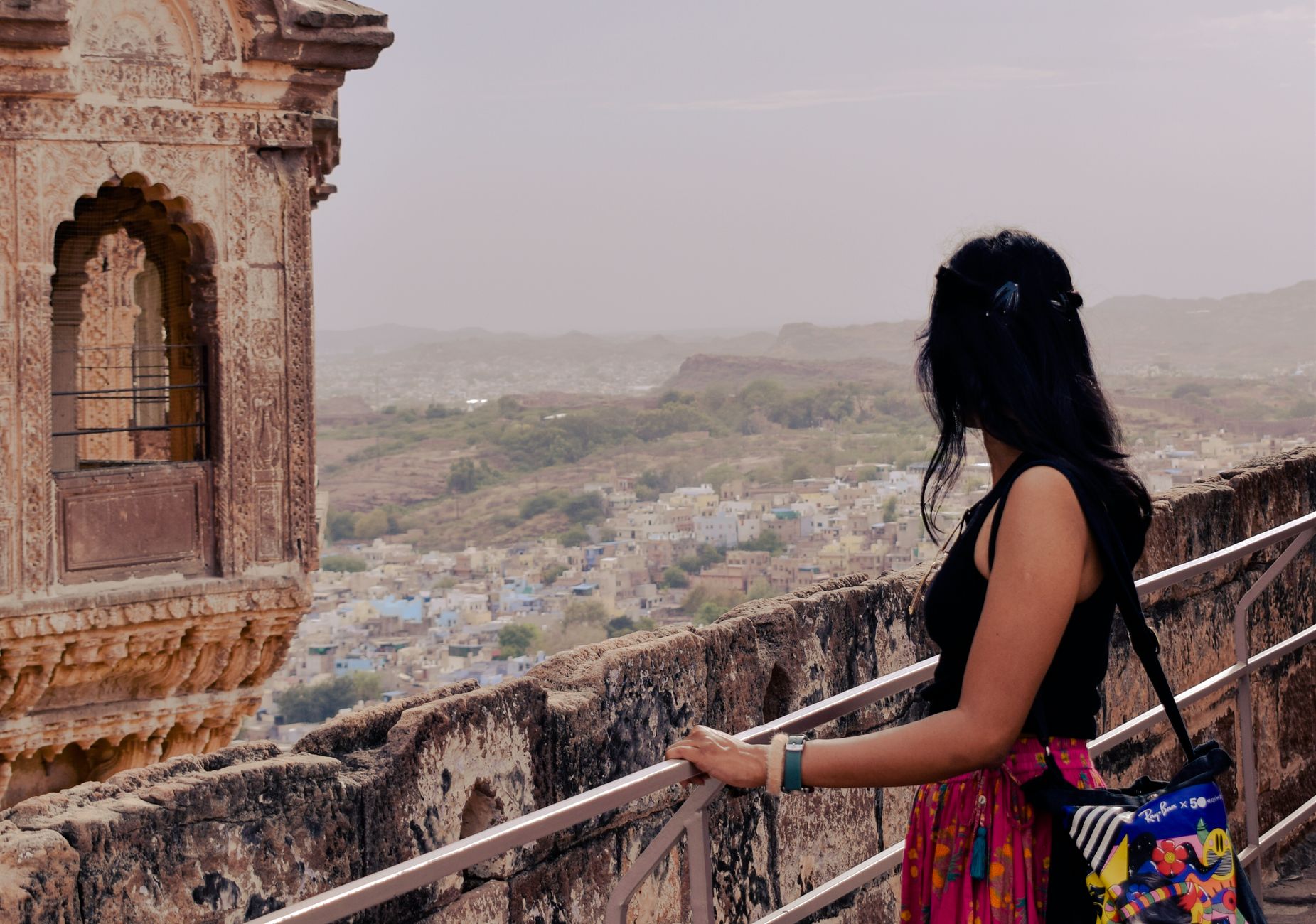A woman gazes over a cityscape from an ancient fort, capturing a blend of history and modern life.