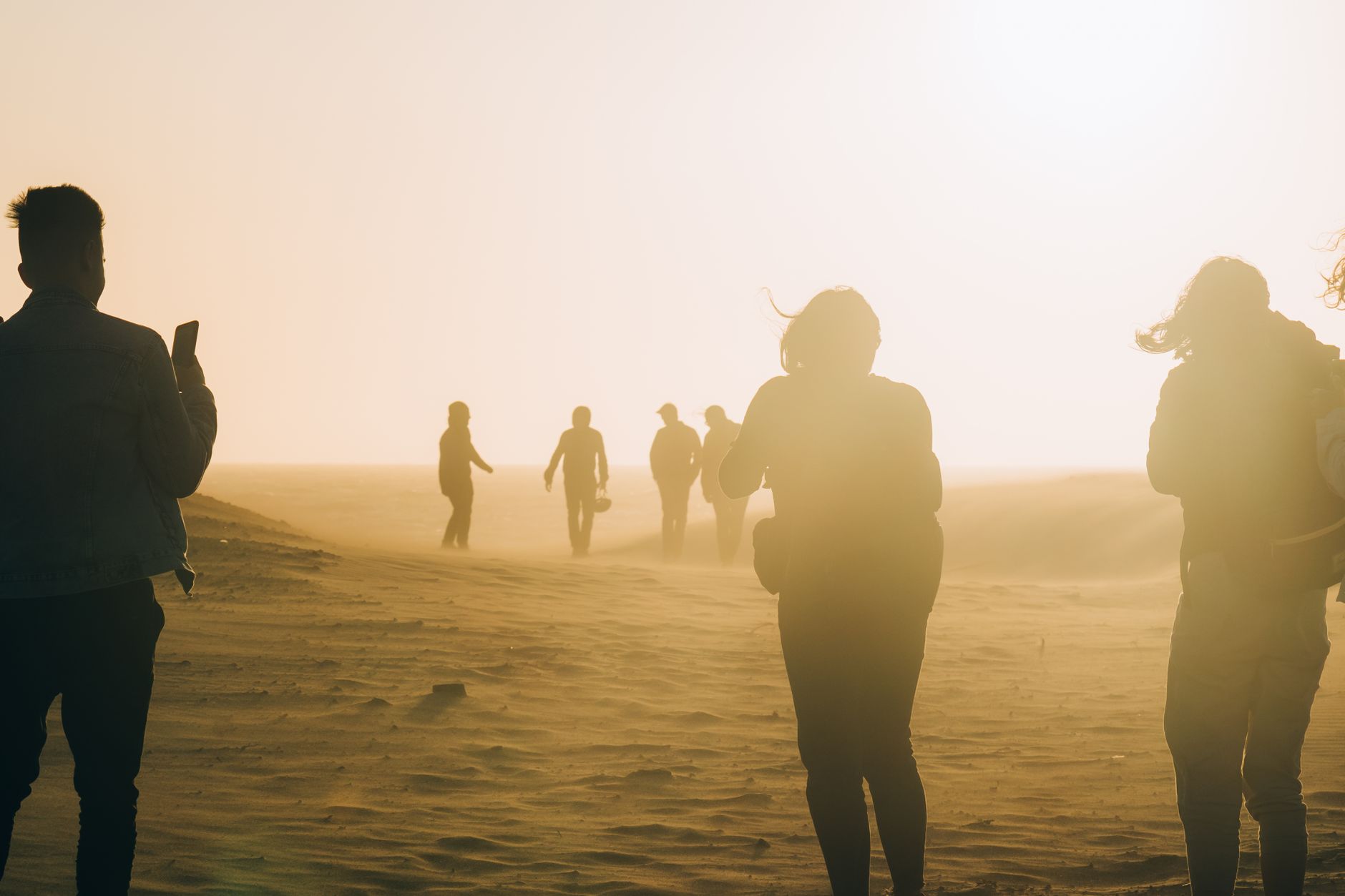 Group of people silhouetted walking through a windy desert at sunset, creating an adventurous mood.