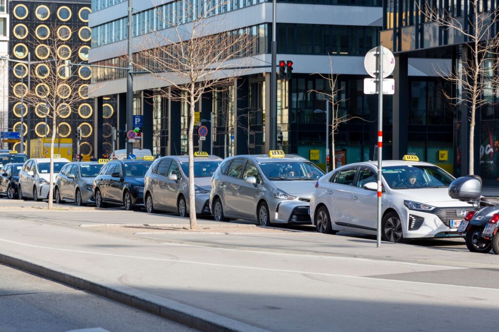 A lineup of taxis on an urban street with modern buildings in the background.